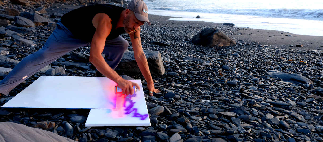 Joe Webster spray-painting landscape graffiti on the beach